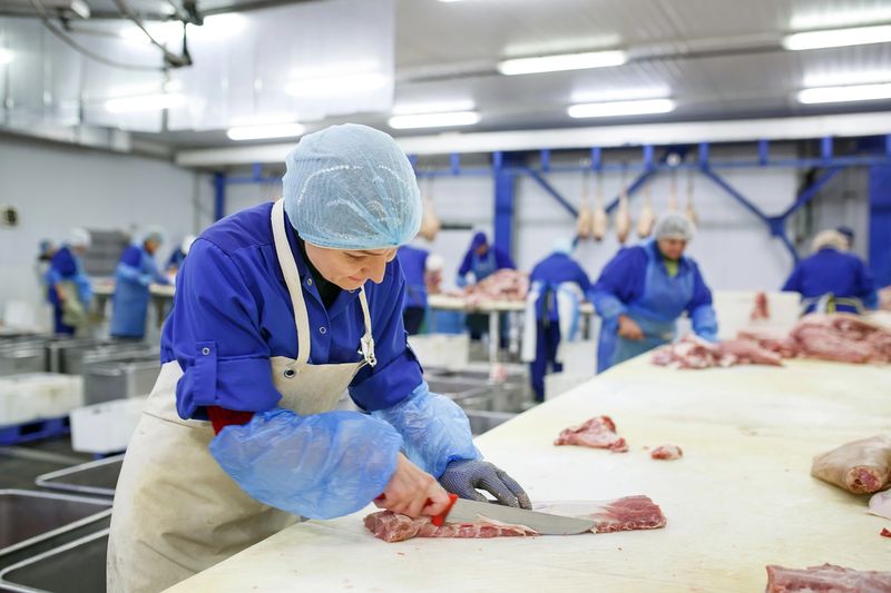 Travailleurs équipés découpant de la viande dans une usine alimentaire
